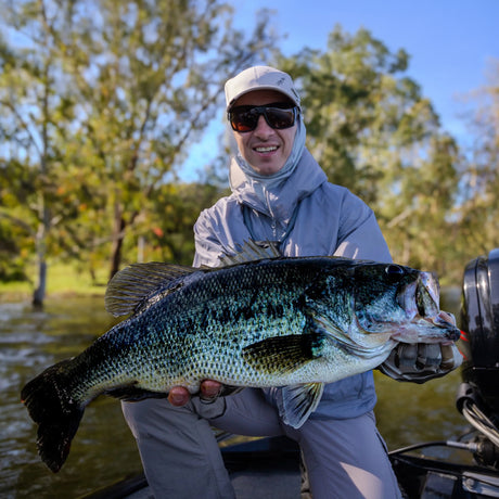 Sportfiskare med solglasögon och keps håller stor fisk vid vattnet i Extremadura, Spanien - fiskeresa och äventyr.