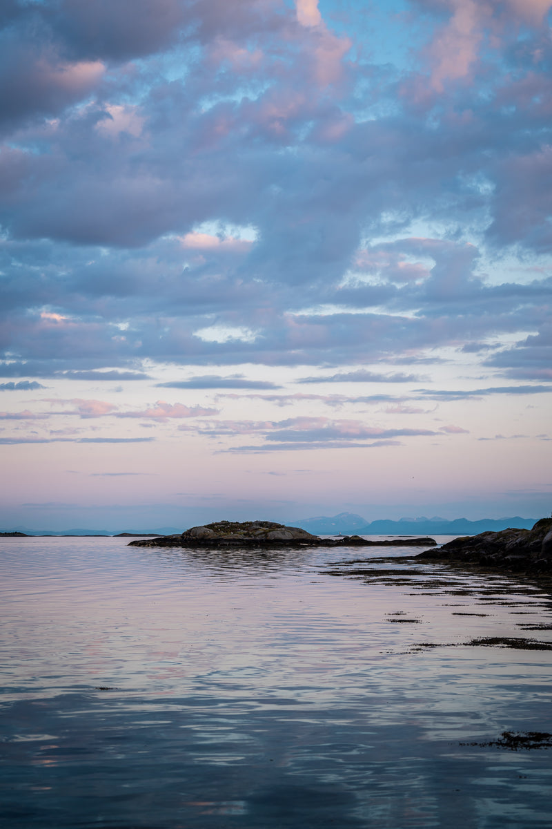 Ett lugnt hav med små klippöar under en delvis molnig himmel vid solnedgången, med rosa och blå reflektioner på vattenytan – perfekt för en avkopplande fisketur eller ett fiskeäventyr.