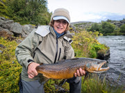 Fiskare håller upp en stor öring vid en strömmande älv på fiskeresa till Island