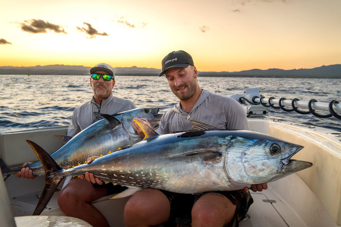 Två fiskare håller upp varsin blåfenad tonfisk vid solnedgången – tonfiskfiske i Spanien utanför Ebrodeltat