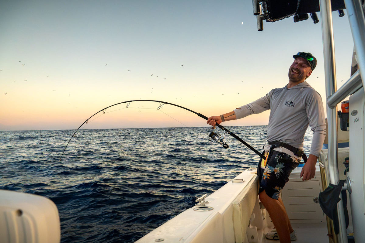 Skrattande fiskare drillar en tonfisk från båten i skymningen med fåglar över havet