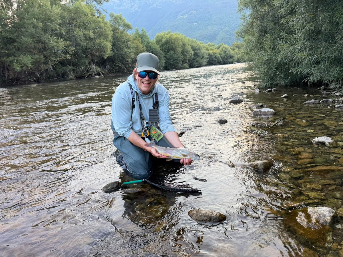 Fröhlicher Fliegenfischer kniet mit einer auf Fliege gefangenen Äsche im Fluss in Montenegro