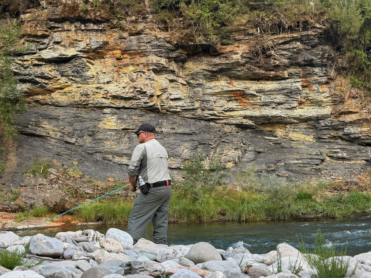 Fliegenfischer wirft vor einer geschichteten, mehrfarbigen Felswand an einem Fluss in Montenegro