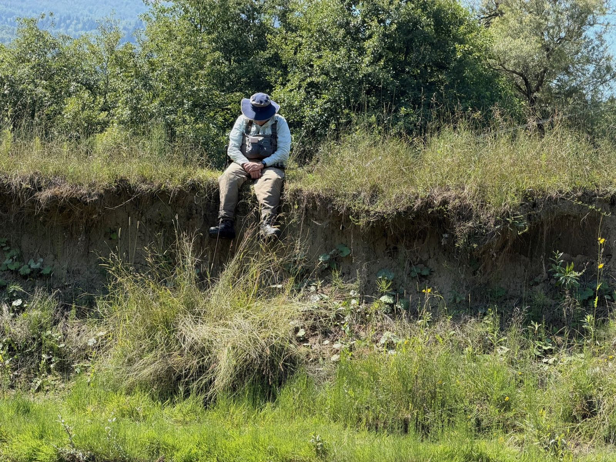 Fliegenfischer mit Sonnenhut sitzt am Flussufer und macht in der Hitze in Montenegro eine Pause