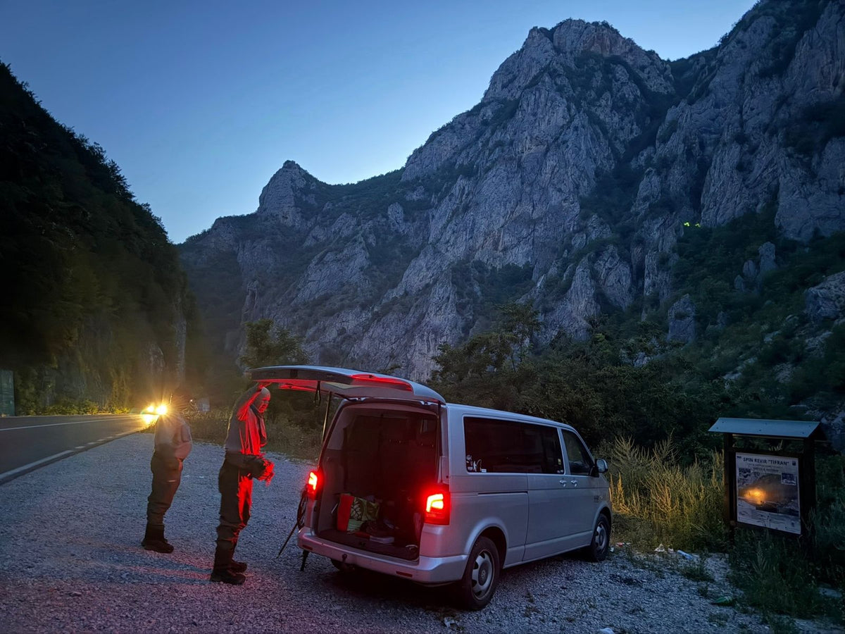 Fliegenfischer in Wathose neben einem Minibus in der Dämmerung unterhalb steiler Berge bei Tifran in Montenegro